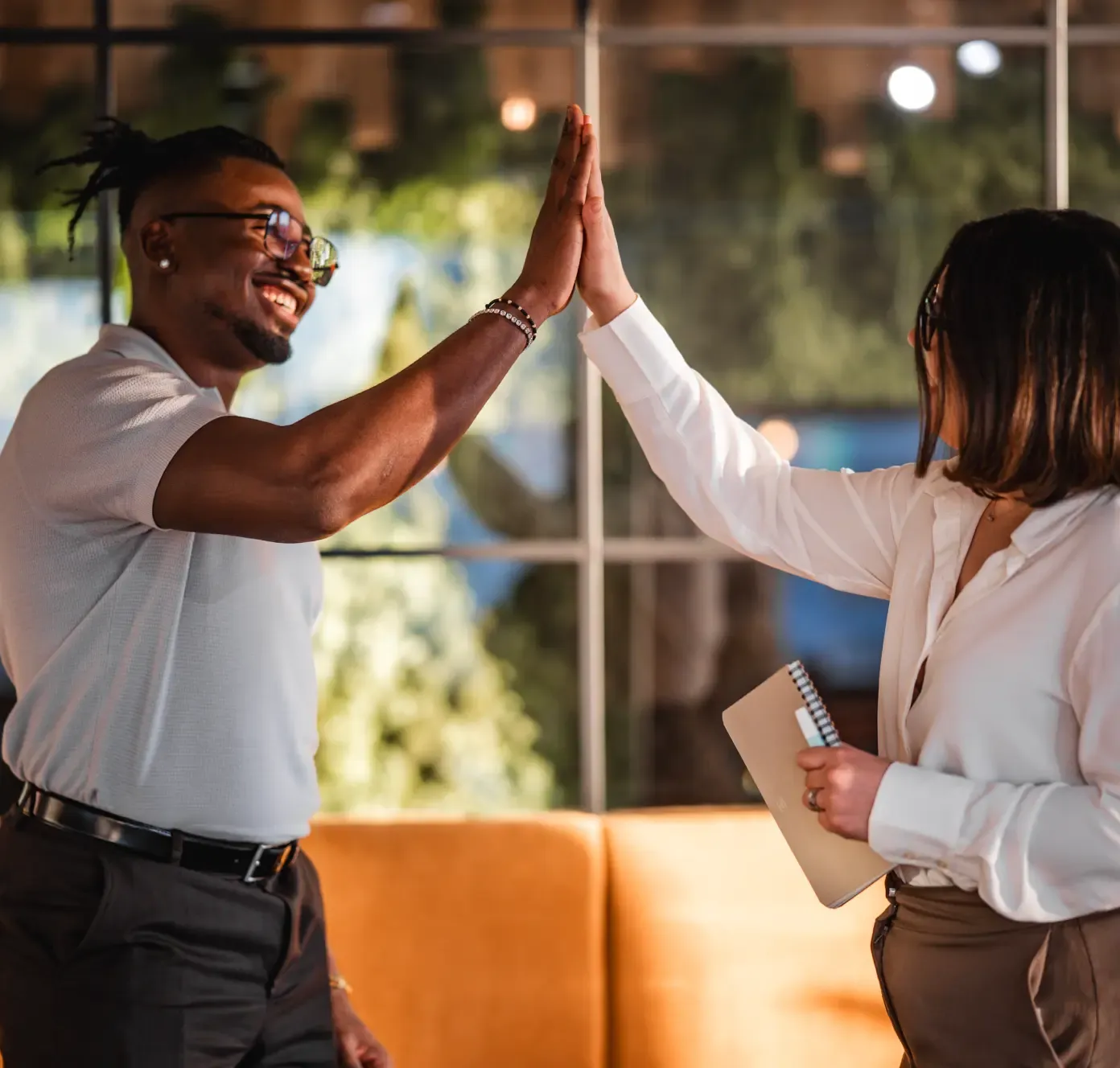 Two colleagues smiling and giving each other a high five in a modern office setting.
